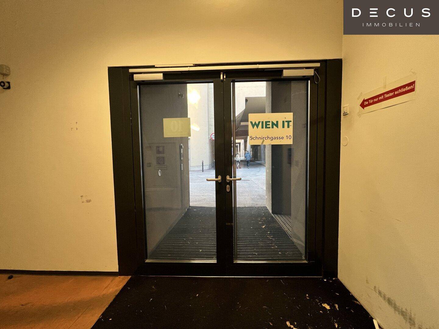 Eingangsbereich mit Glastüren und einem Schild, das auf die Adresse hinweist.