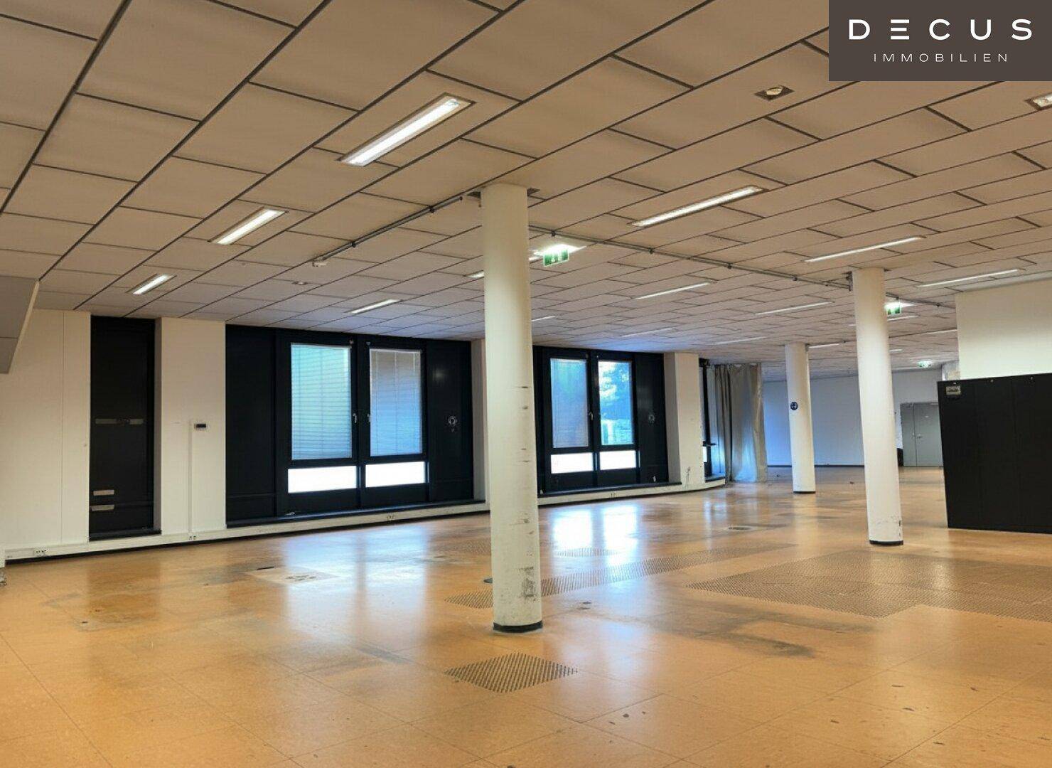 Geräumiger Bürobereich mit mehreren Säulen, großen Fenstern und heller Deckenbeleuchtung.