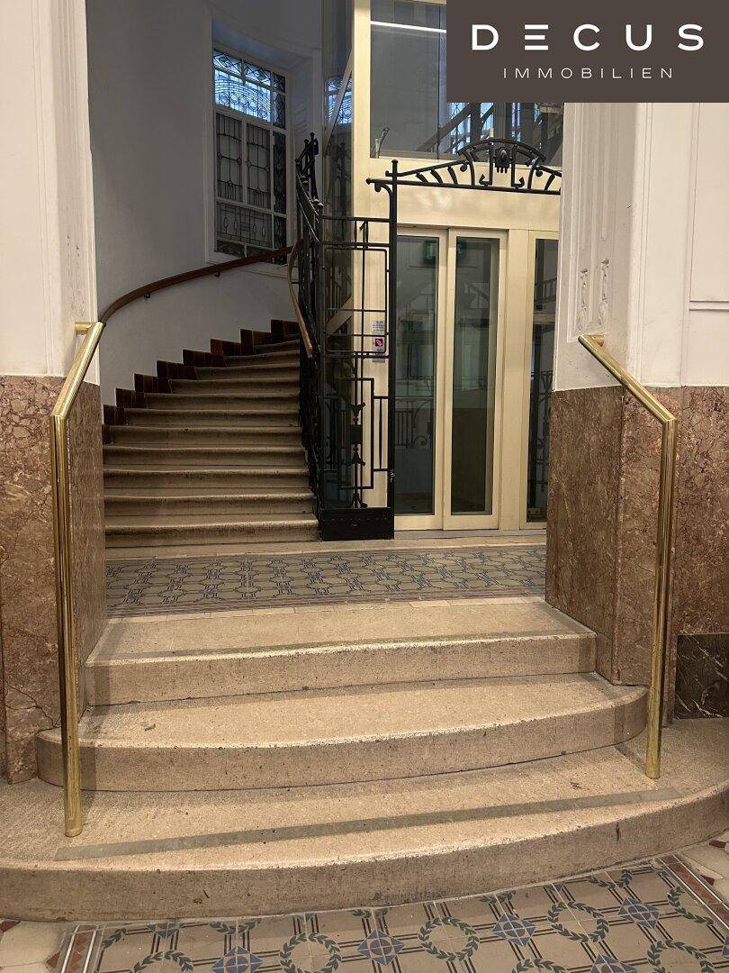 Elegantes Treppenhaus mit Marmorstufen, goldenen Handläufen und einem modernen Glasaufzug.