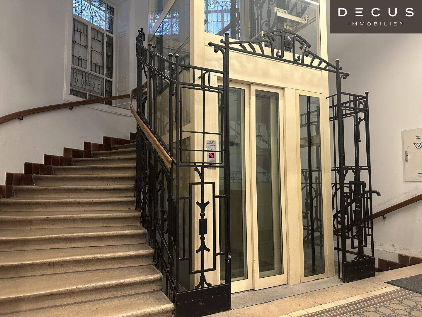 Geräumiges Treppenhaus mit geschwungener Treppe, kunstvollem Geländer und einem eleganten Aufzug.
