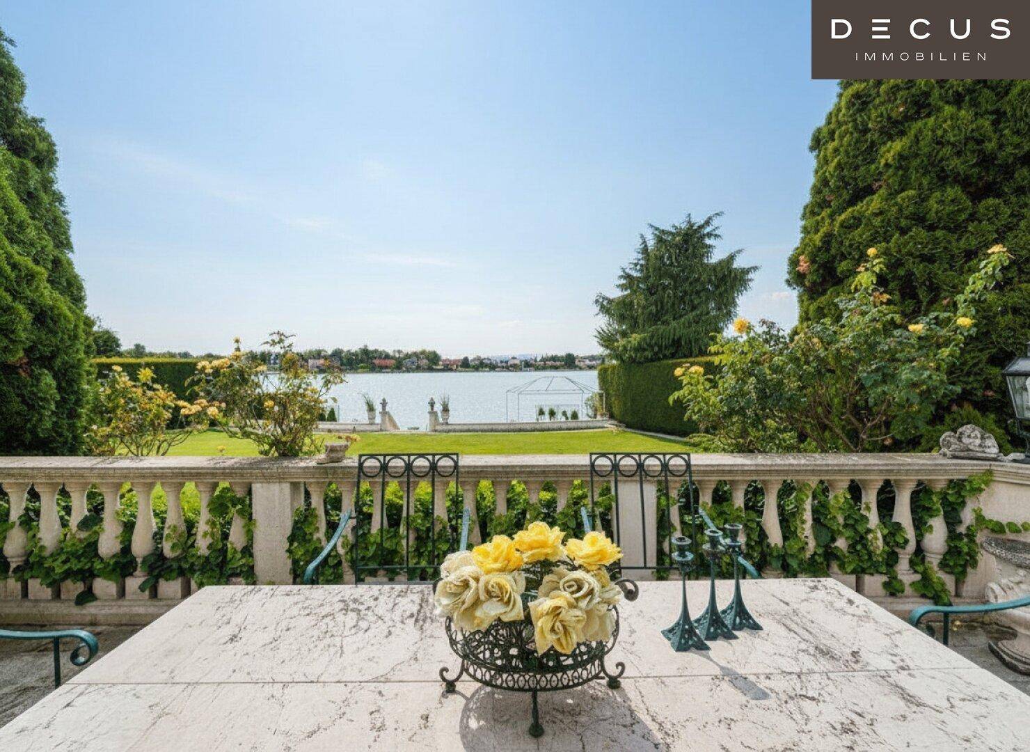 Gemütlicher Essbereich auf der Terrasse mit Blick auf den See und üppiger Bepflanzung.