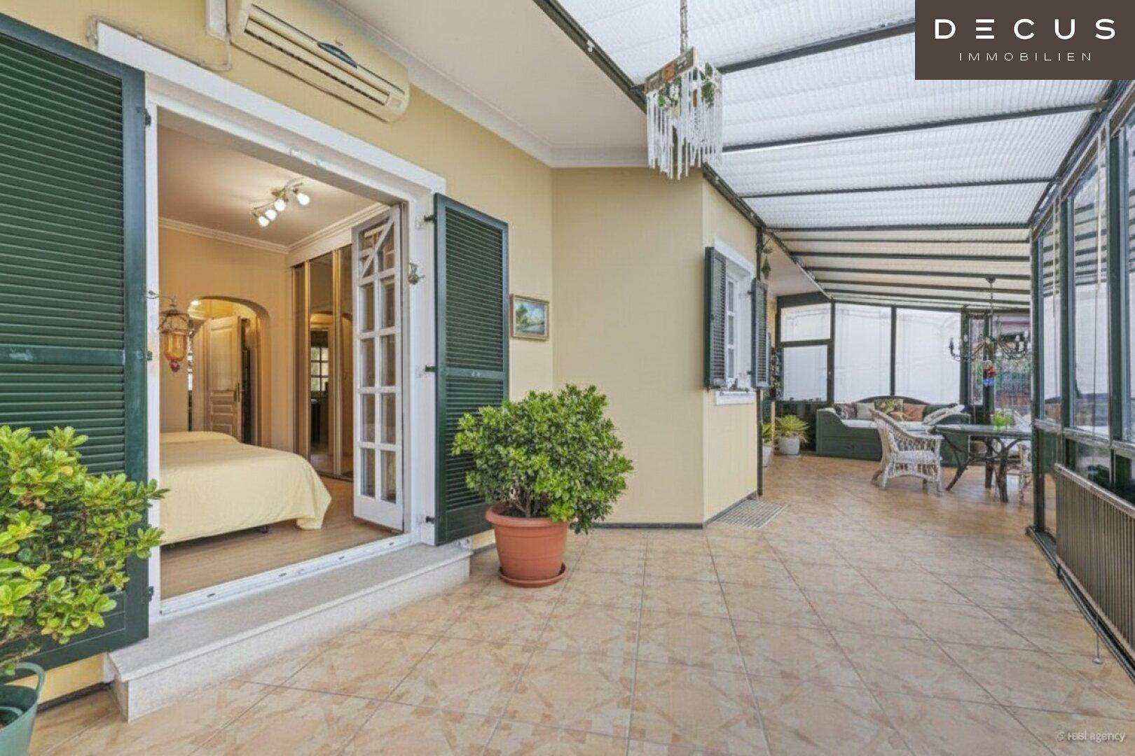 Große überdachte Terrasse mit Fliesenboden, Zugang zum Schlafzimmer und Blick in den Wintergarten.
