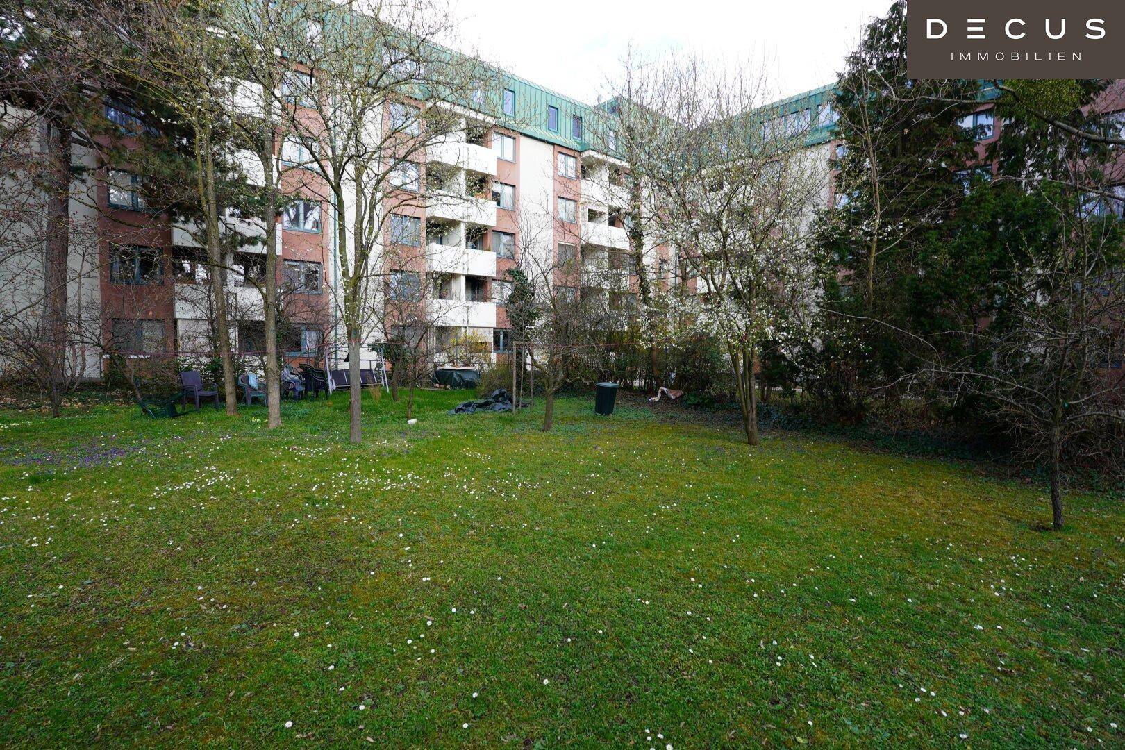 Gepflegte Grünfläche mit Rasen und Bäumen vor einem Mehrfamilienhaus.