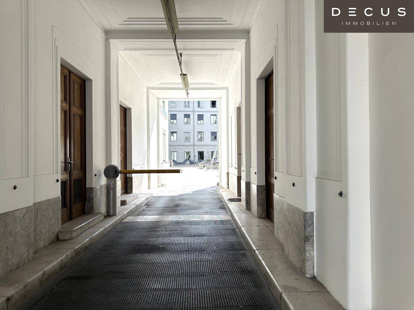 Einfahrt zu einem Parkbereich mit Schranke und hohen Decken in einem Gebäude mit klassischer Architektur.