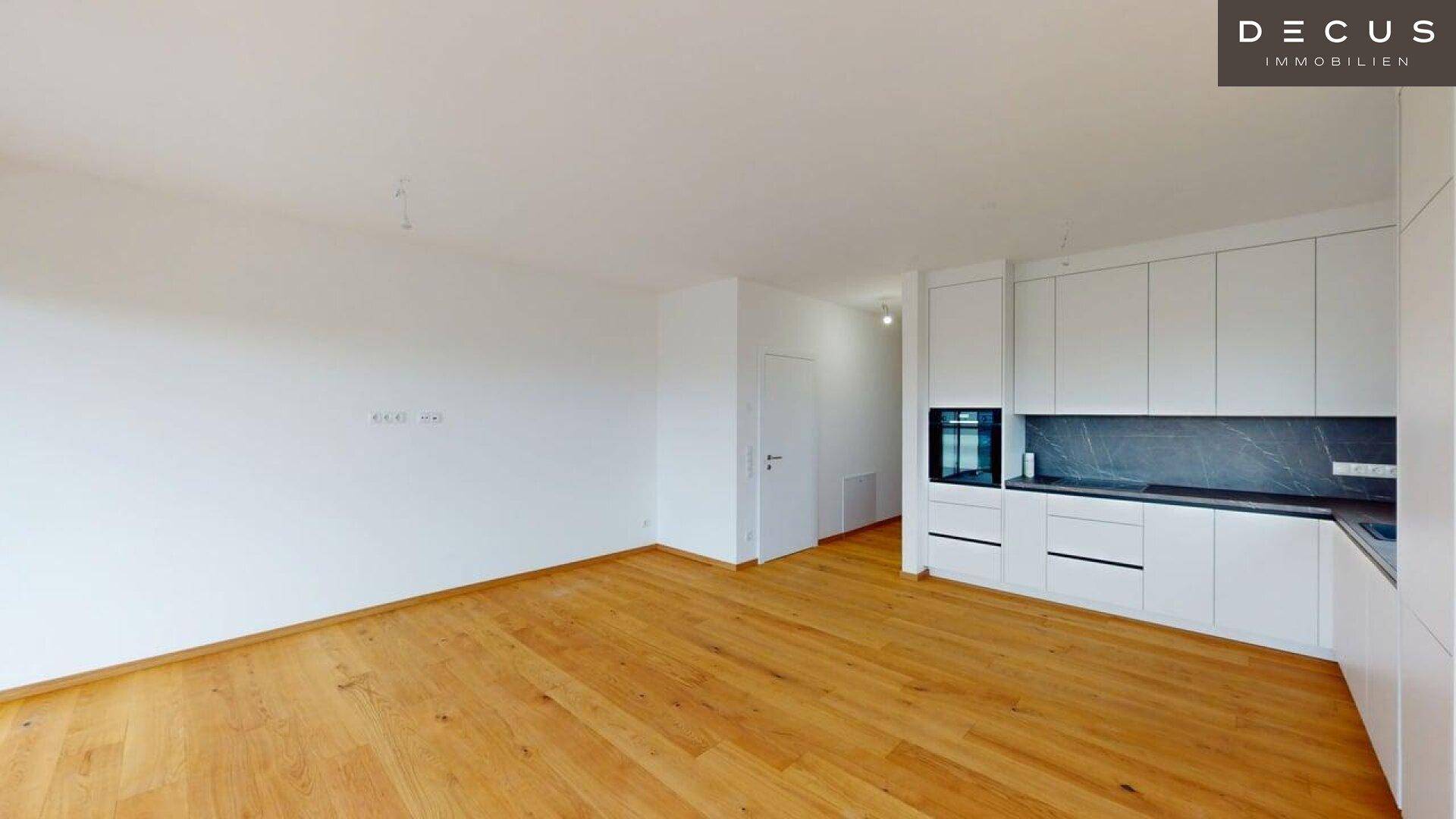 Moderner Wohnbereich mit integrierter weißer Küche und hellem Parkettboden.