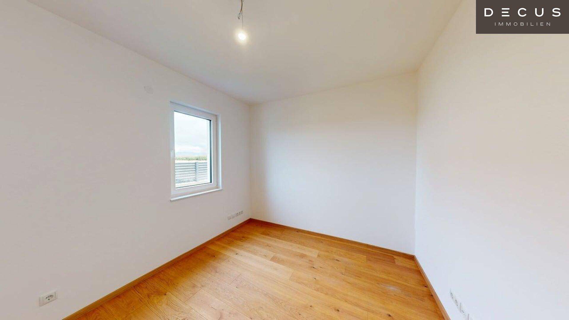 Helles Schlafzimmer mit Holzboden und einem Fenster, das viel Tageslicht hereinlässt.