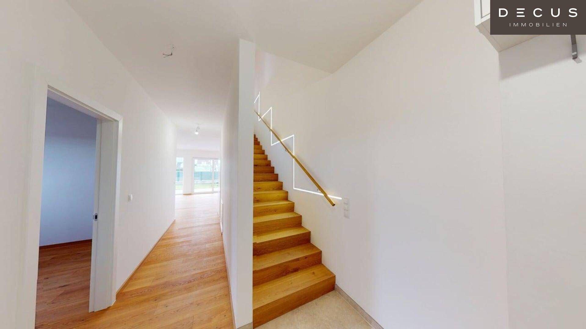 Eingangsbereich mit moderner Holztreppe und indirekter Beleuchtung, die zum Obergeschoss führt.