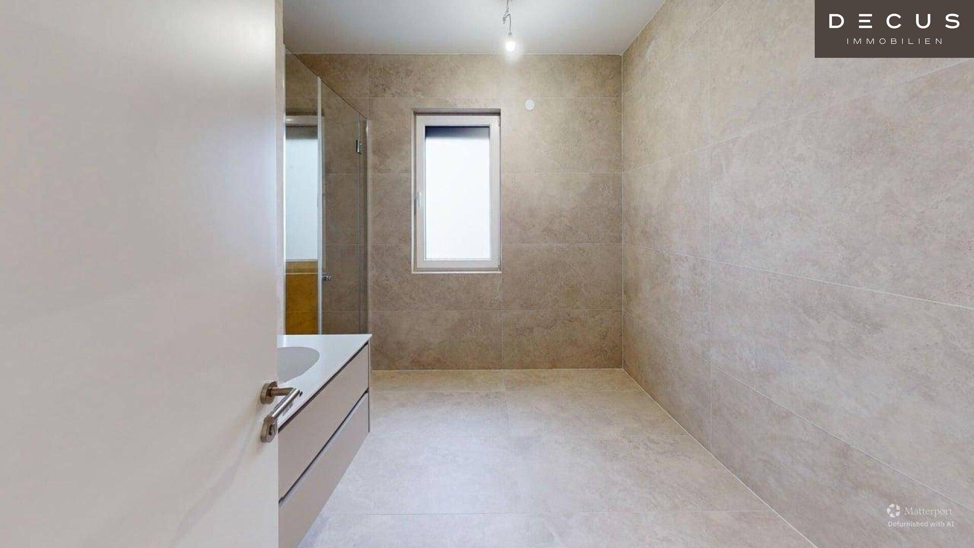 Modernes Badezimmer mit hellen Fliesen, Fenster und Platz für eine Dusche.
