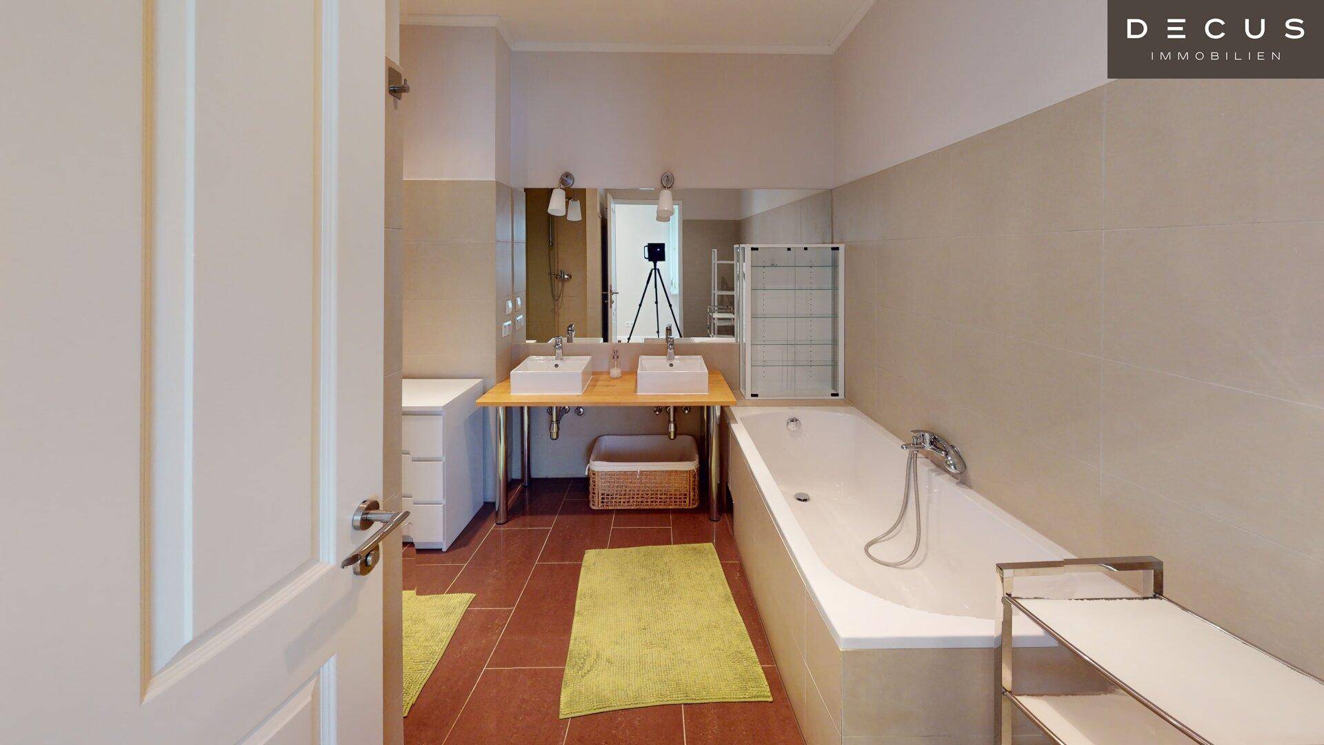 Helles Badezimmer mit Badewanne, Doppelwaschbecken und gelben Akzenten.
