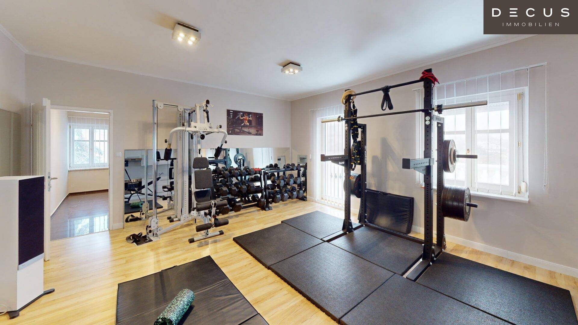 Gut ausgestatteter Fitnessraum mit Hanteln, Kraftgeräten und großen Spiegeln.