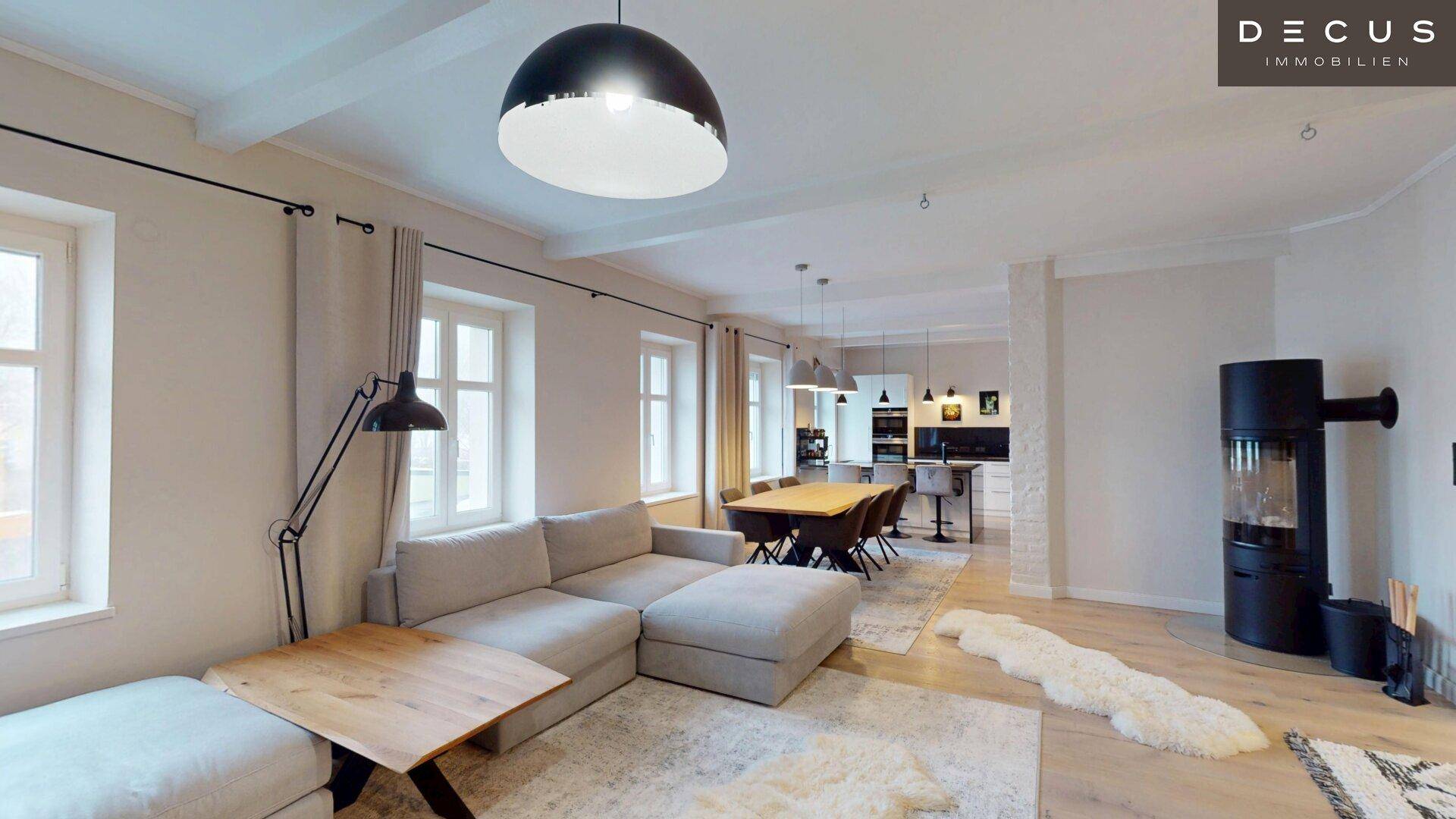 Offener Wohn- und Essbereich mit großem Sofa, Kaminofen und Blick auf die Küche.