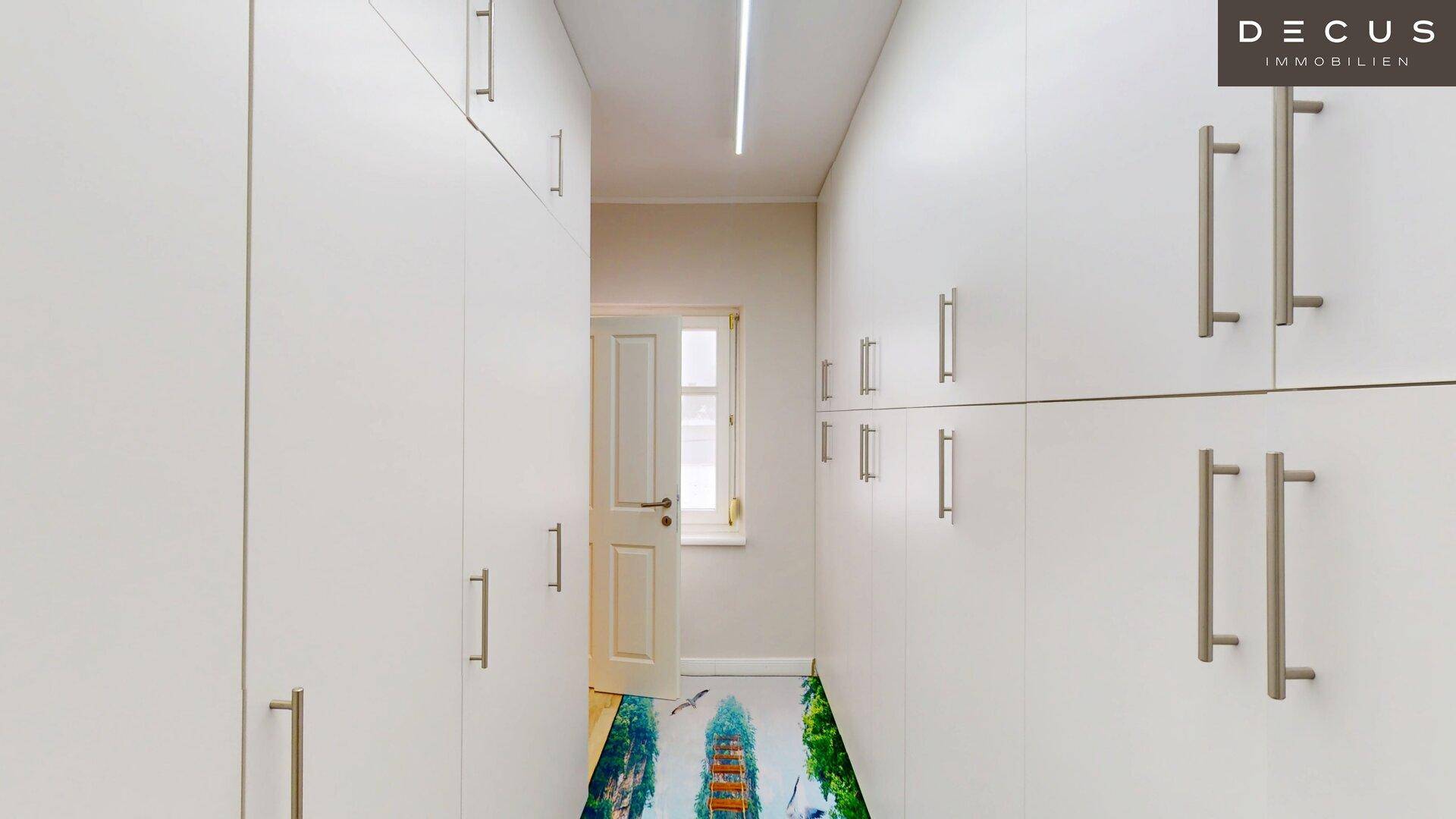Praktischer begehbarer Kleiderschrank mit vielen weißen Einbauschränken und Fenster.