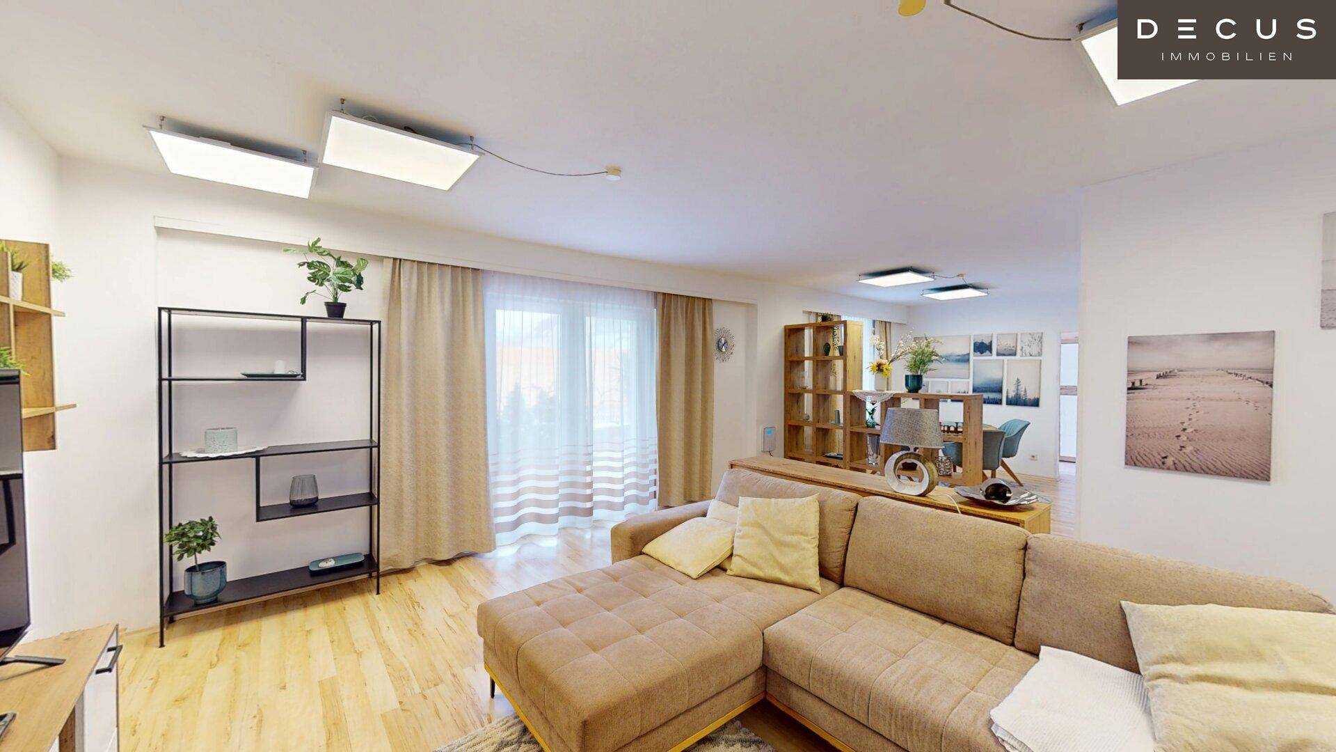 Offener Wohn-Essbereich mit Sofa, Regalen und großen Fenstern.