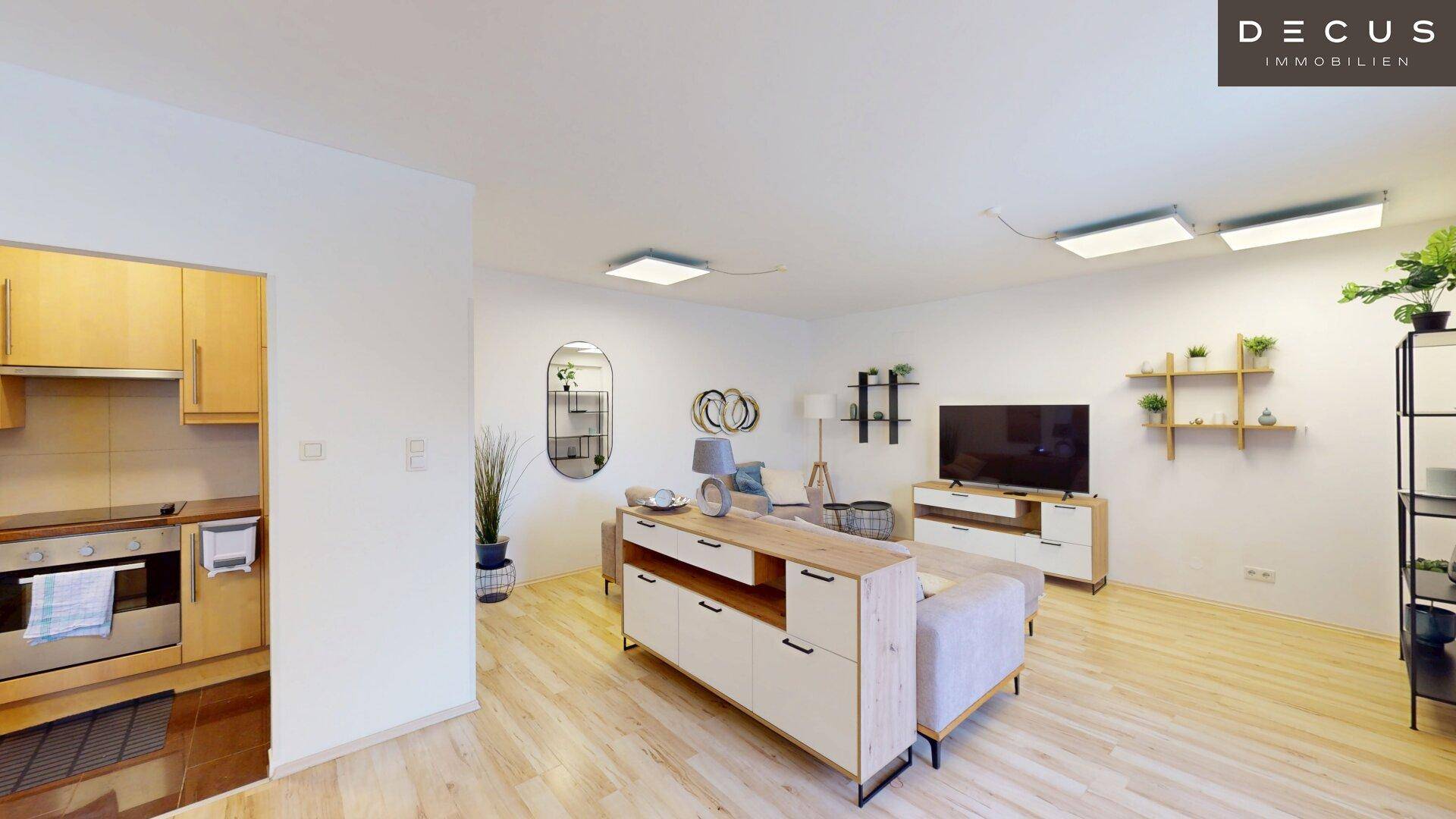 Heller Wohnbereich mit Sofa, TV-Möbeln und integrierter Küchenzeile im Hintergrund.