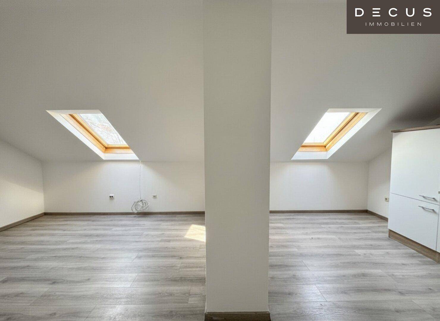 Großzügiger Dachgeschossraum mit zwei Dachfenstern und hellem Laminatboden, ideal für Wohnzwecke.
