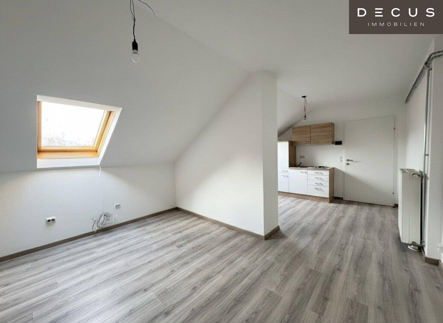 Offener Wohnbereich im Dachgeschoss mit integrierter Küchenzeile und hellem Laminatboden.