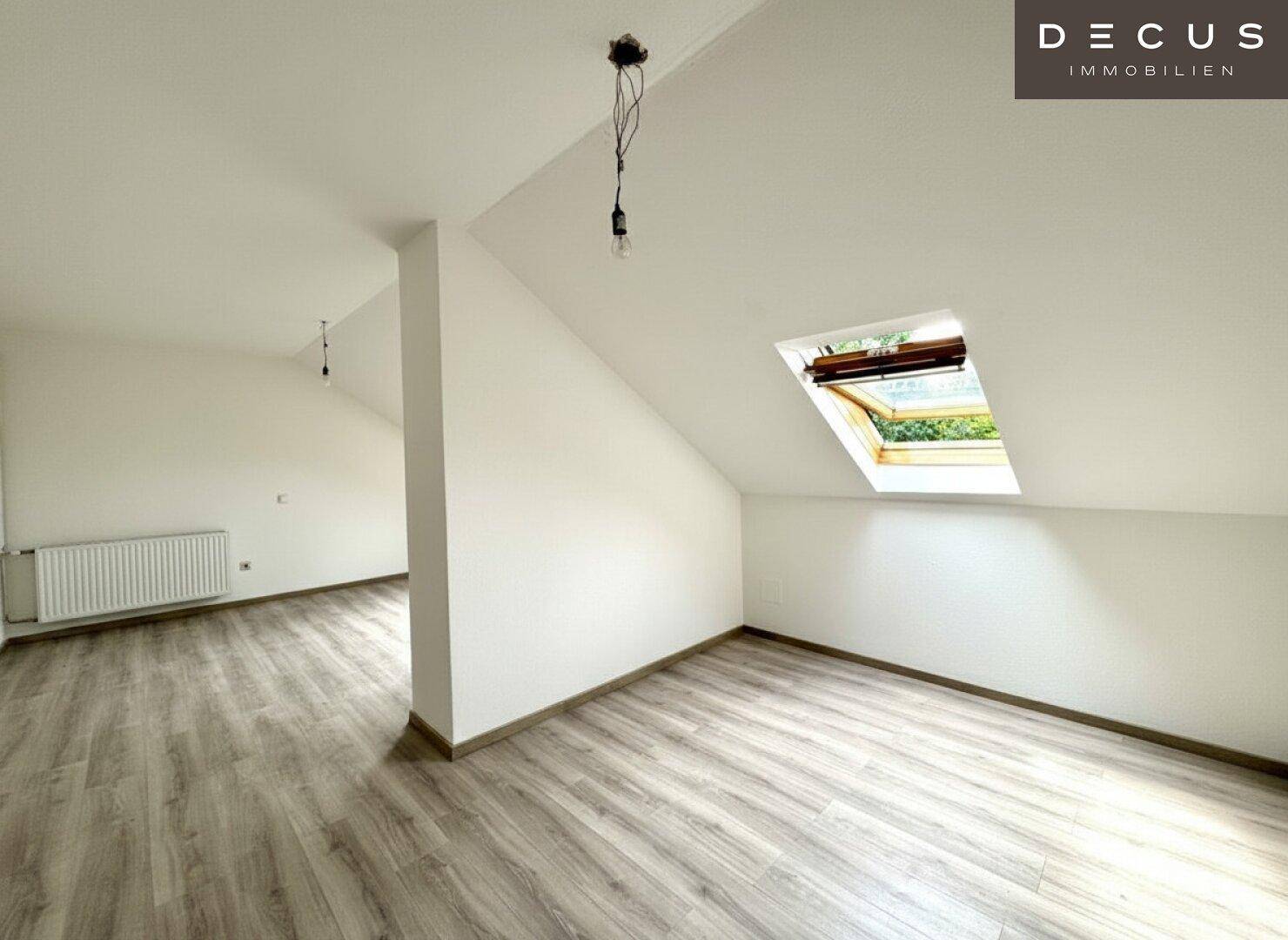 Heller Wohnbereich im Dachgeschoss mit Laminatboden, Dachfenster und Heizkörper.