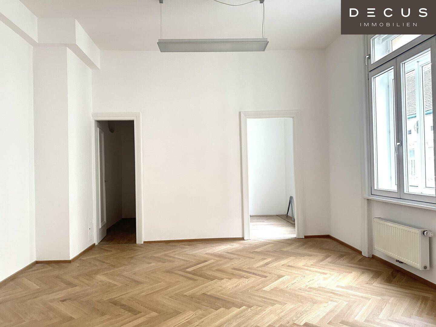 Leerer Raum mit Fischgrätparkett und zwei Türöffnungen, bietet vielseitige Nutzungsmöglichkeiten.