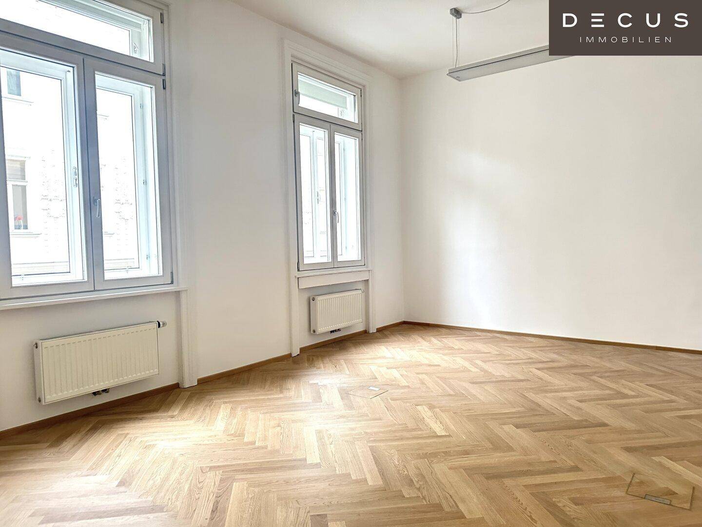 Heller Raum mit Fischgrätparkett, hohen Fenstern und Heizkörpern, ideal für verschiedene Einrichtungsstile.