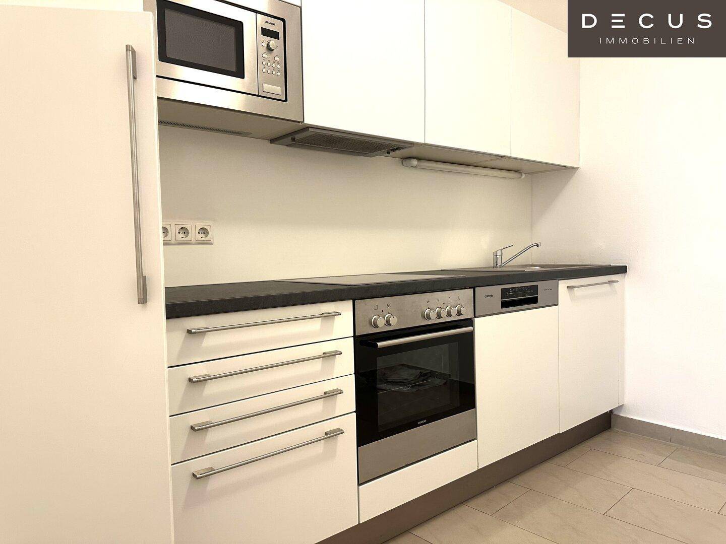 Moderne Einbauküche mit weißen Schränken, dunkler Arbeitsplatte und integrierten Geräten.