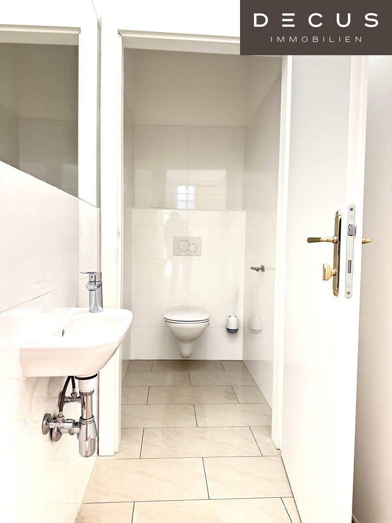 Helles Gäste-WC mit wandhängendem WC, kleinem Waschbecken und weißen Fliesen.