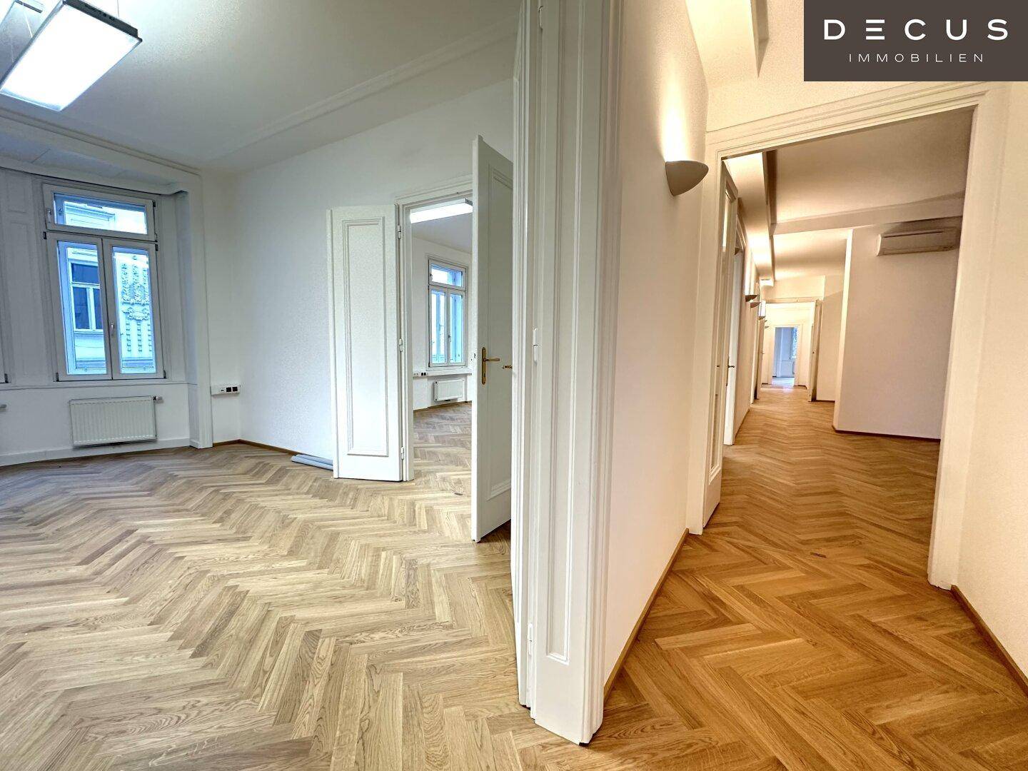 Blick vom Raum in den langen Flur mit Fischgrätparkett und vielen Türen, hell und geräumig.