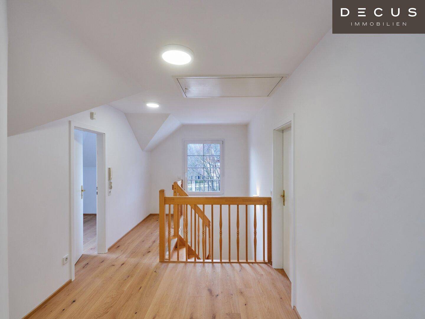 Heller Flur im Obergeschoss mit Holzgeländer und Fenster, das Tageslicht hereinlässt.