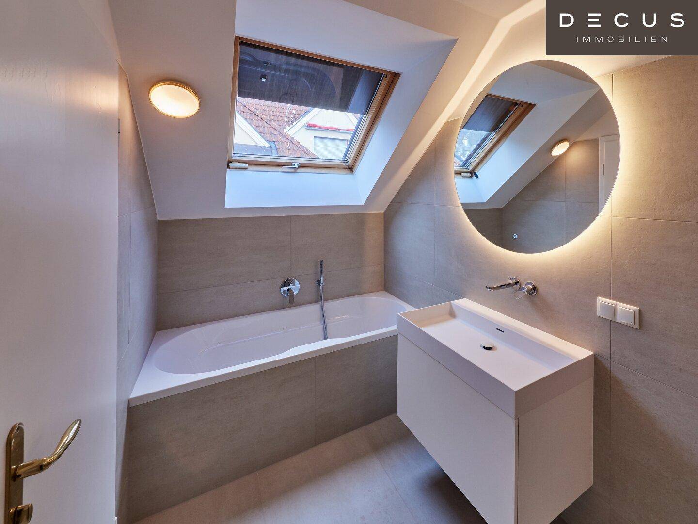 Helles Badezimmer mit Badewanne, modernem Waschtisch und Dachfenstern für viel Tageslicht.