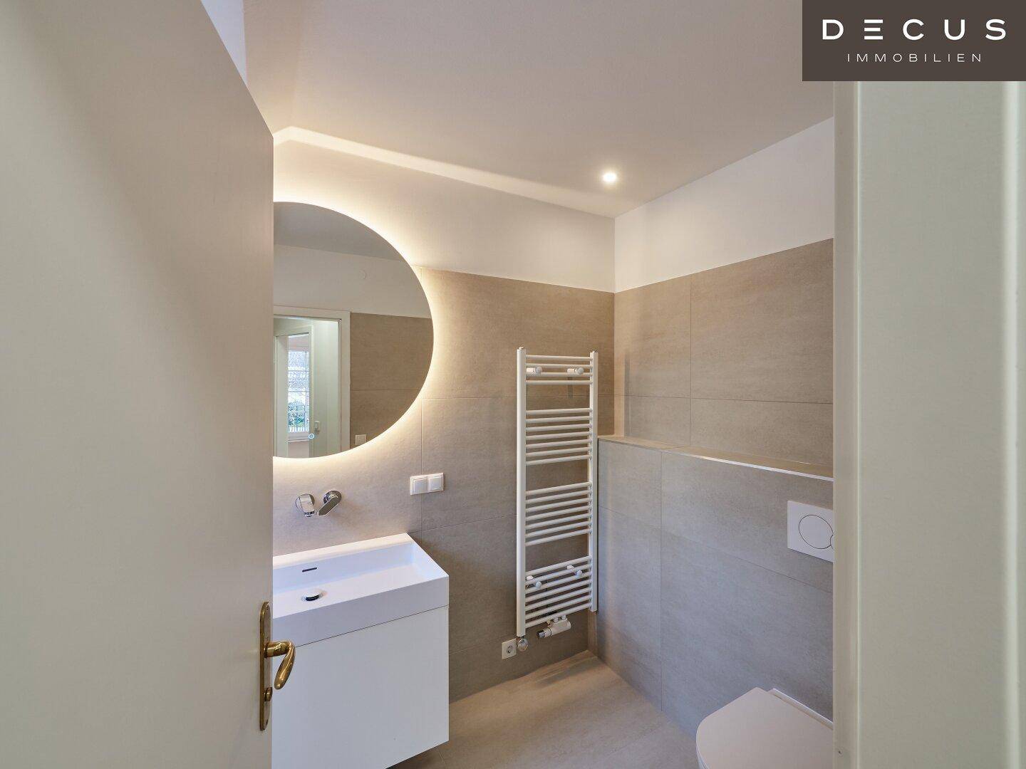 Modernes Badezimmer mit beleuchtetem Spiegel, Einzelwaschbecken und beheiztem Handtuchhalter.