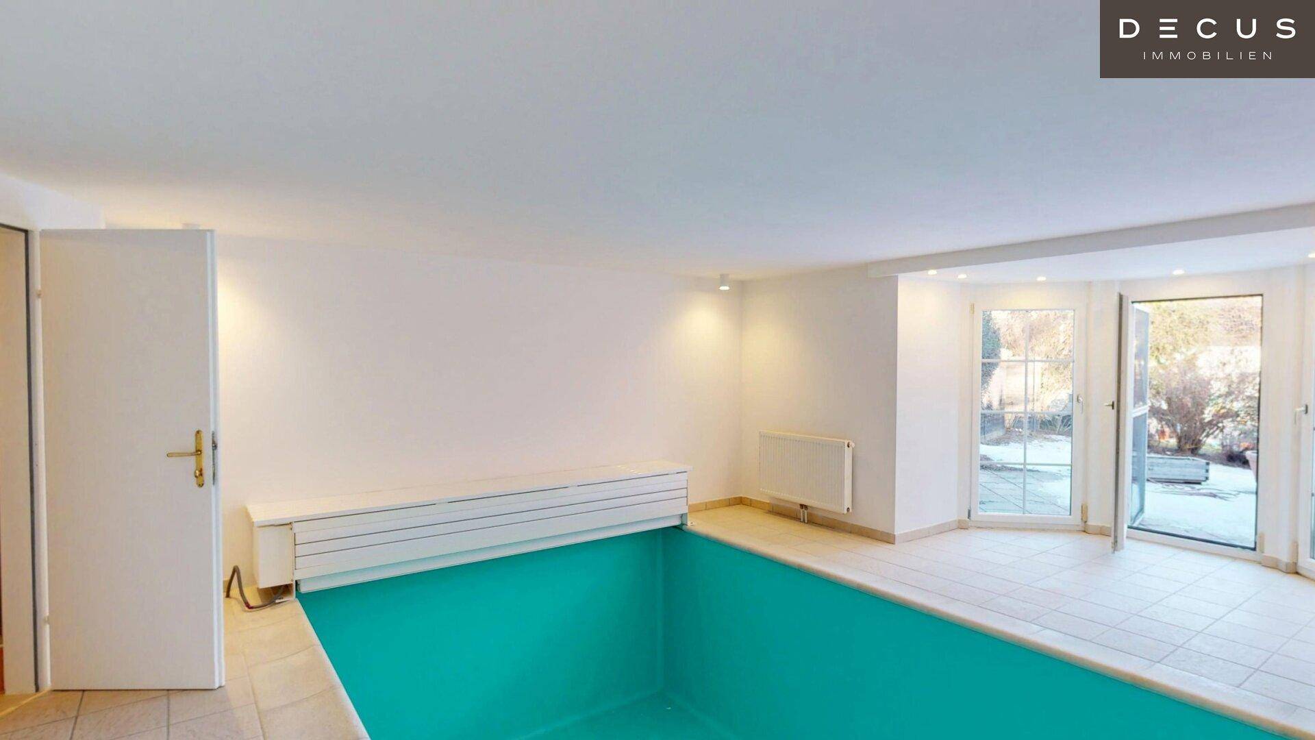 Innenpoolbereich mit hellen Fliesen und Zugang zum Außenbereich durch große Fenster.