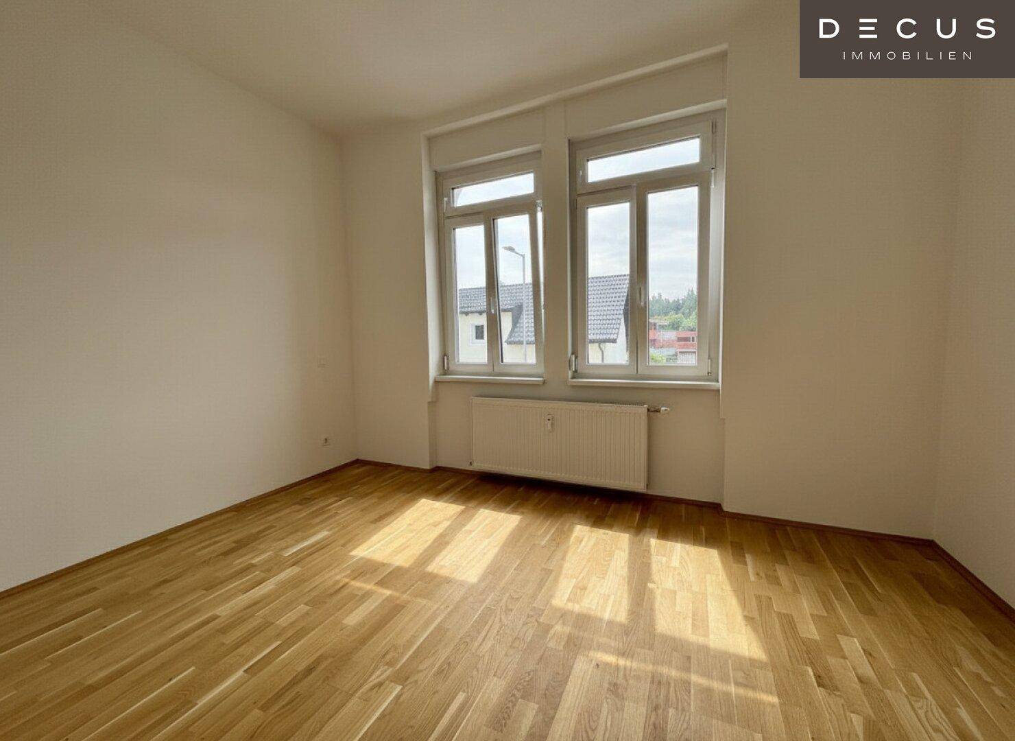 Leerer Raum mit Holzboden und großen Fenstern, ideal für Schlafzimmer oder Büro.