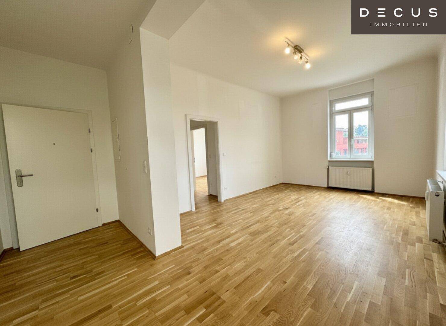 Geräumiger, leerer Wohnbereich mit Holzboden und viel Tageslicht.