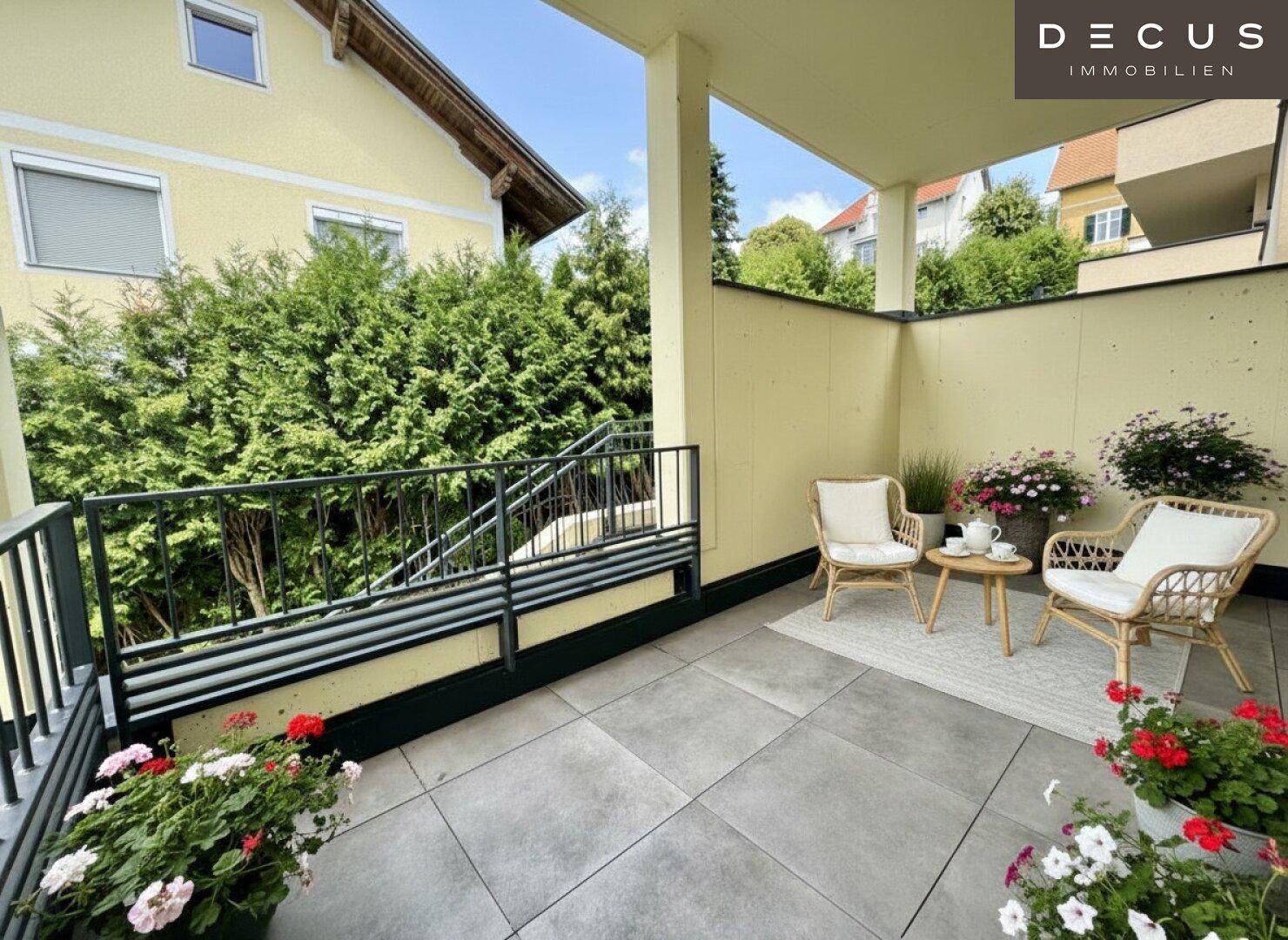 Überdachter Balkon mit Fliesenboden, Gartenmöbeln und Blick ins Grüne.