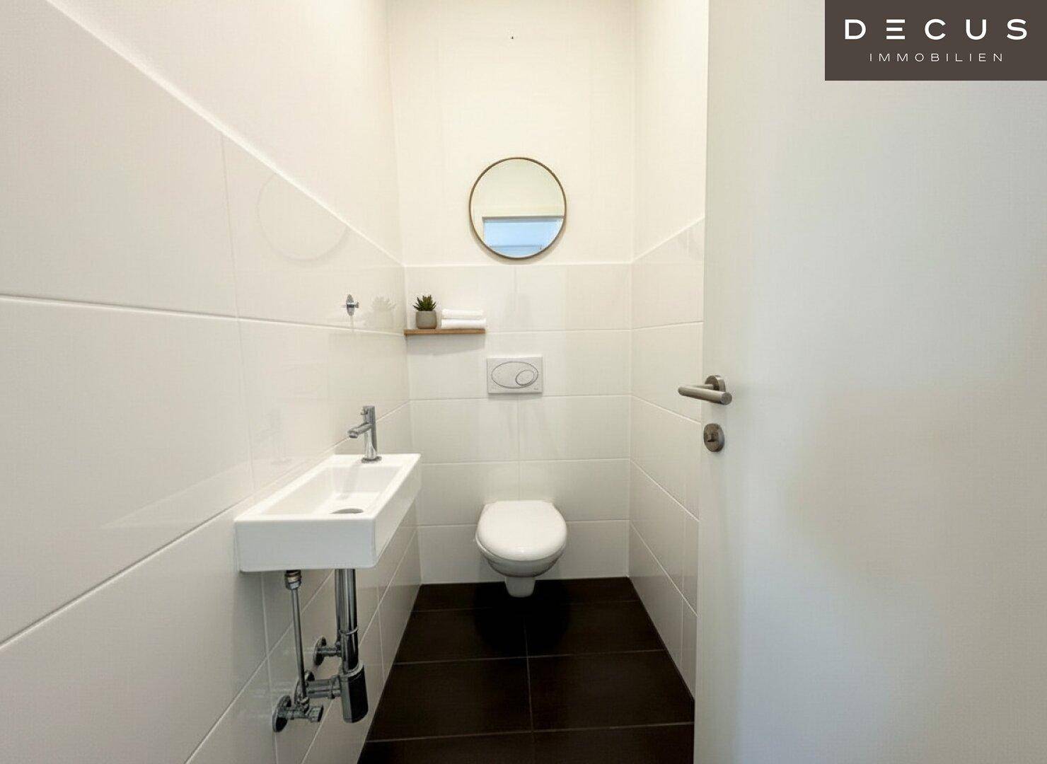Separates Gäste-WC mit Wand-WC, kleinem Waschbecken und Spiegel.