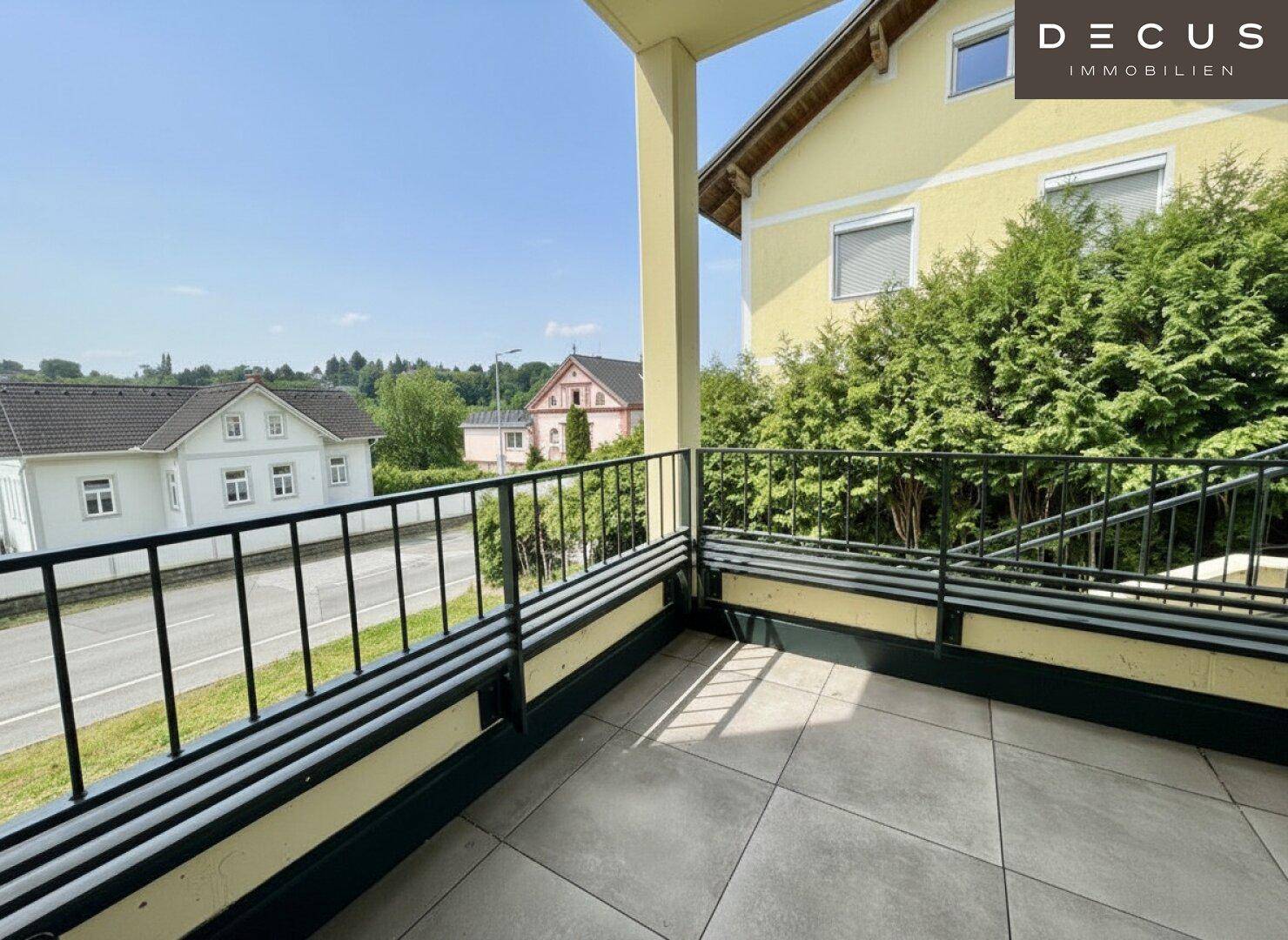 Sonniger Balkon mit Fliesenboden und Blick auf die Straße und umliegende Häuser.