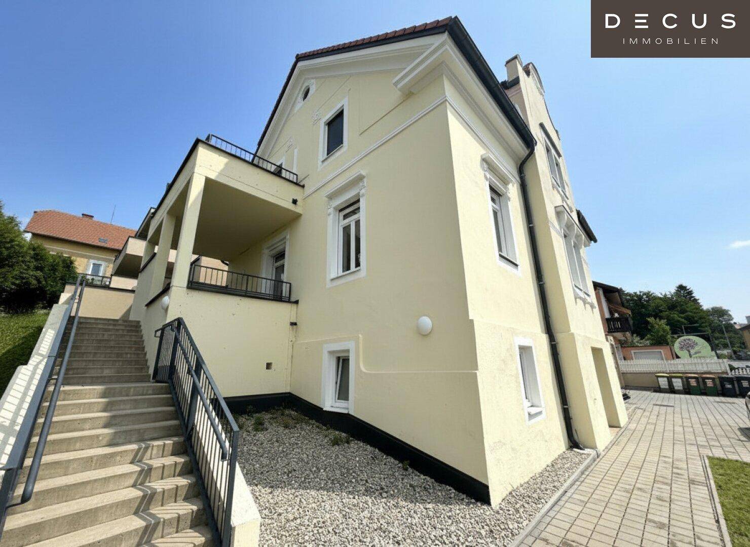 Rückansicht des Gebäudes mit Außentreppe, gelber Fassade und gepflegter Umgebung.