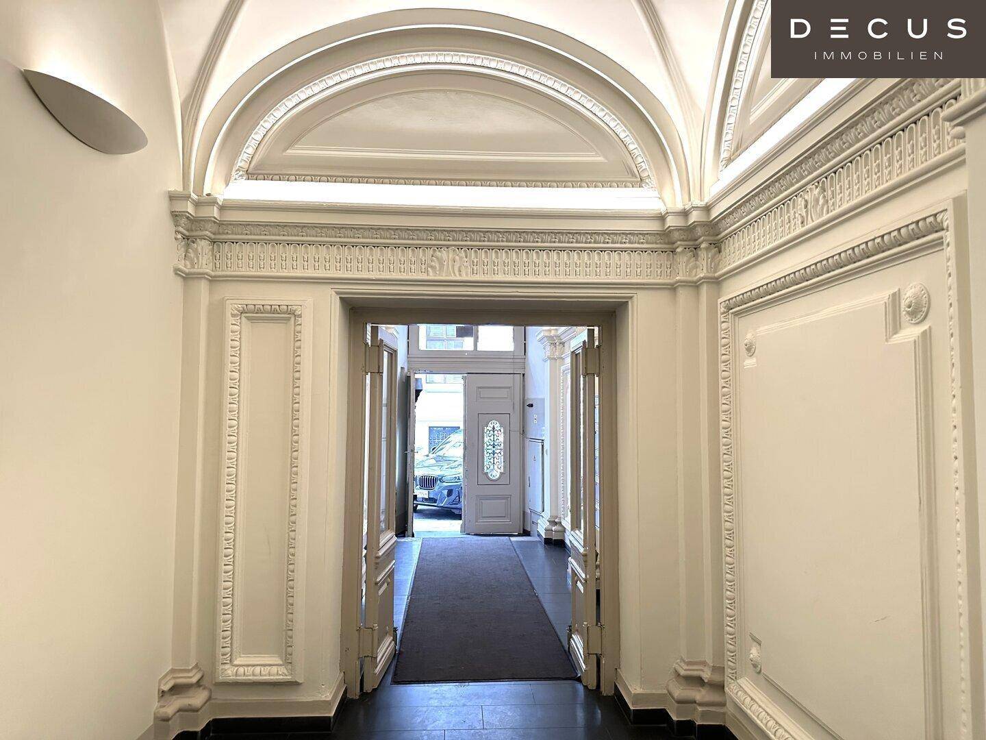 Eleganter Eingangsbereich mit gewölbter Decke und aufwendigen Stuckverzierungen, führt zum Gebäudeausgang.