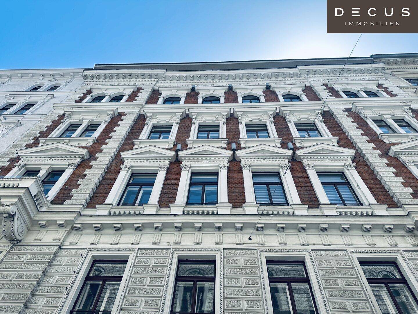 Historische Fassade eines Altbaus mit reich verzierten Fenstern und Ziegeldetails unter blauem Himmel.