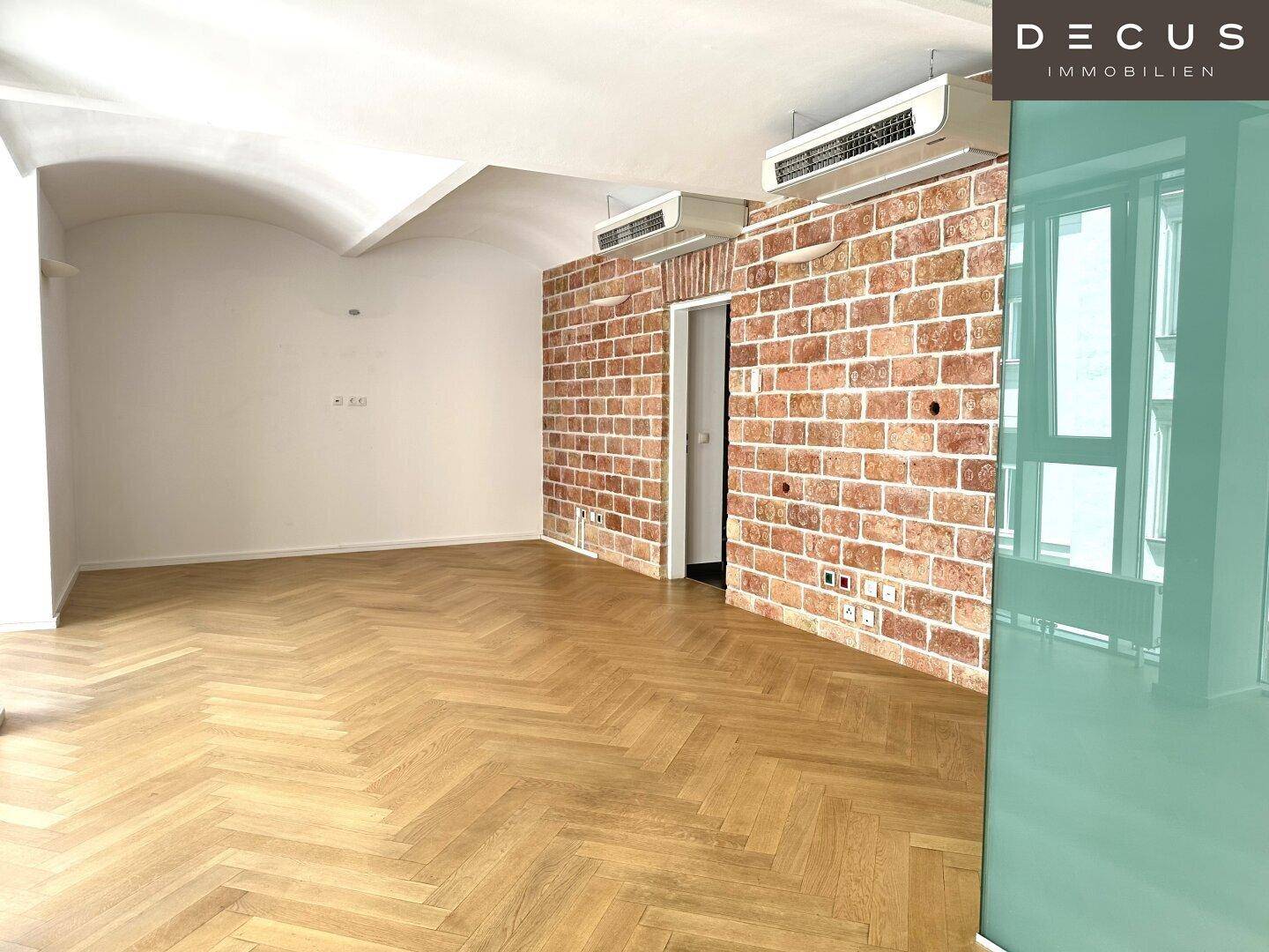 Leerer Konferenzraum mit freiliegender Backsteinwand, gewölbter Decke und Fischgrätparkett.