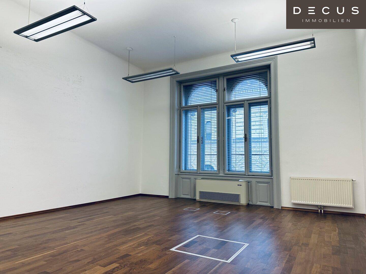 Leeres Büro mit dunklem Holzparkett und großen Fenstern mit Jalousien, bietet viel Raum.