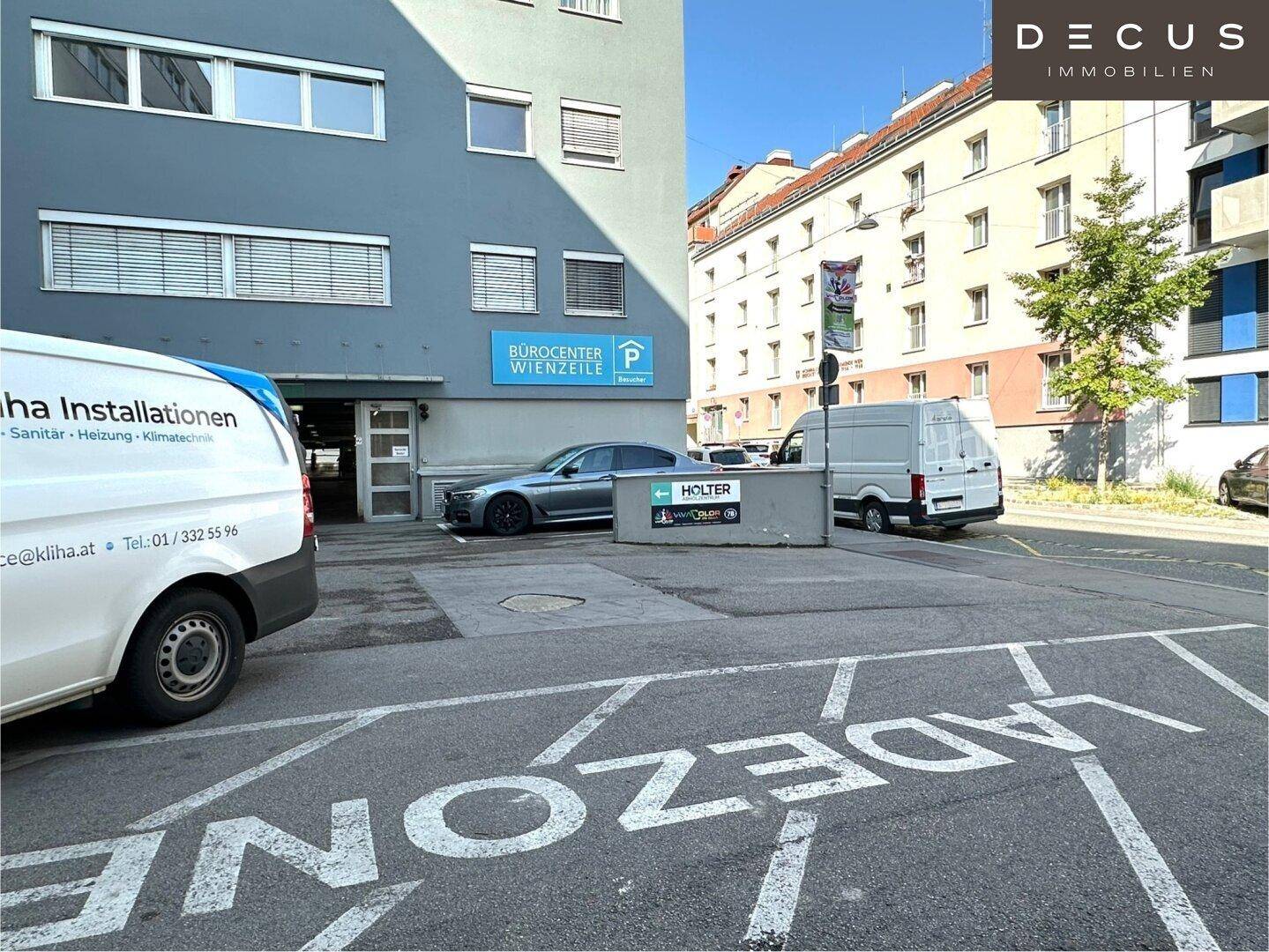 Eingangsbereich eines Bürogebäudes mit Ladezone, geparkten Fahrzeugen und umliegenden Gebäuden.