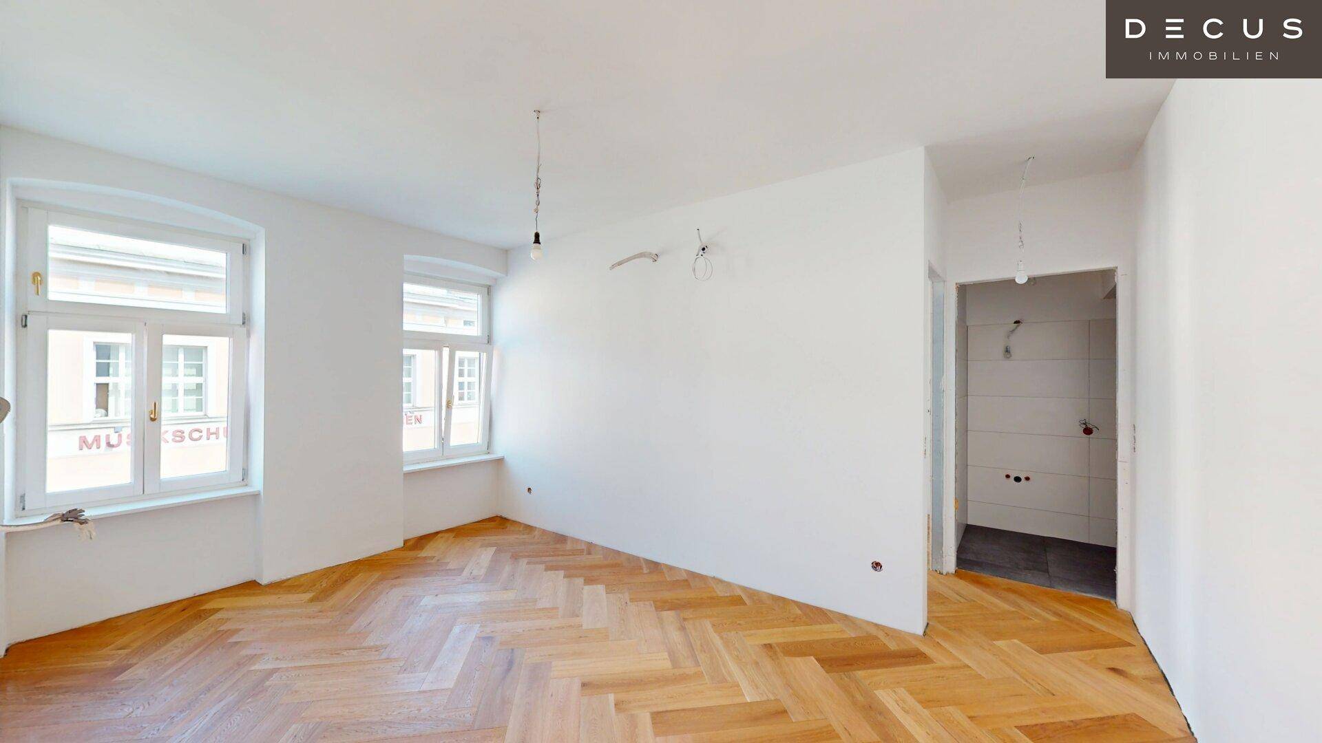 Heller Raum mit Fischgrätparkett und Zugang zu einem im Bau befindlichen Badezimmer.