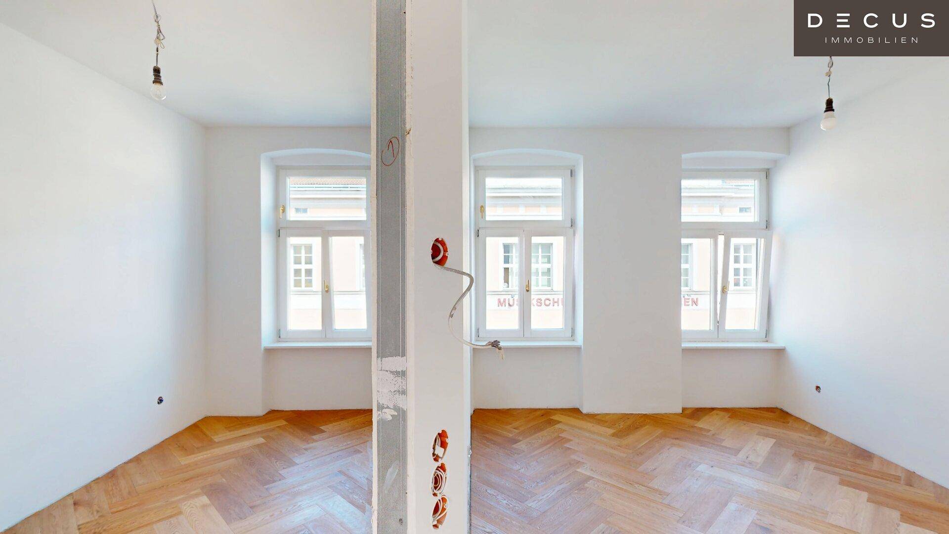 Heller Raum mit Fischgrätparkett und sichtbaren Installationsvorbereitungen für eine Trennwand.