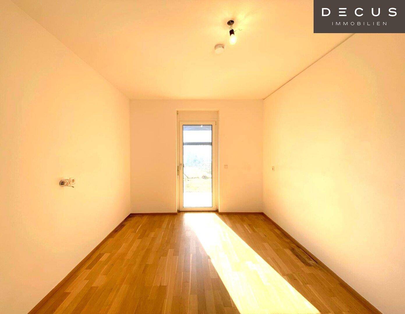 Leeres Schlafzimmer mit hellem Parkettboden und direktem Zugang zu einem Außenbereich.