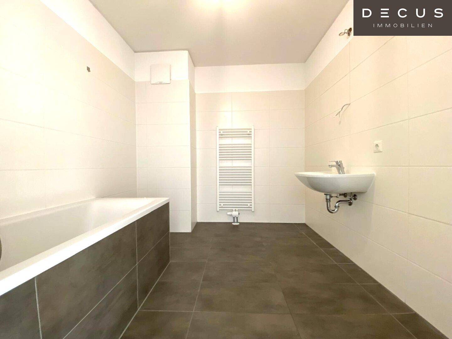 Modernes Badezimmer mit Badewanne, Waschbecken, beheiztem Handtuchhalter und hellen Fliesen.