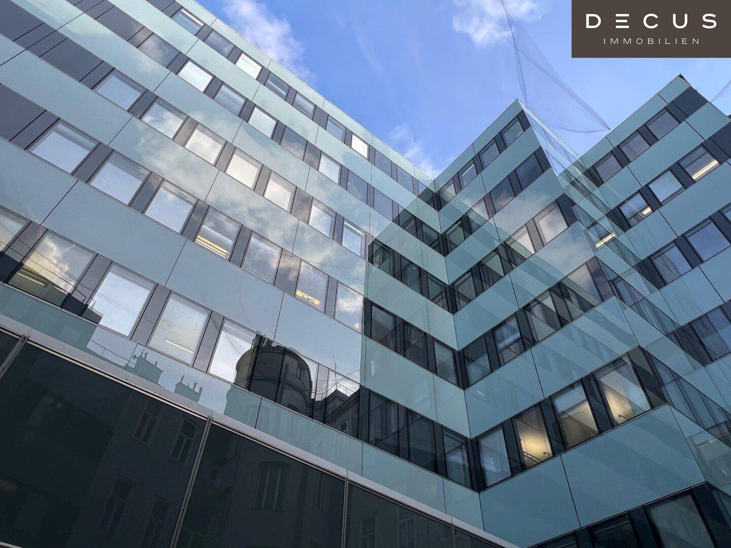 Moderne Bürogebäude-Fassade mit großen Glasflächen und blauen Paneelen unter klarem Himmel.