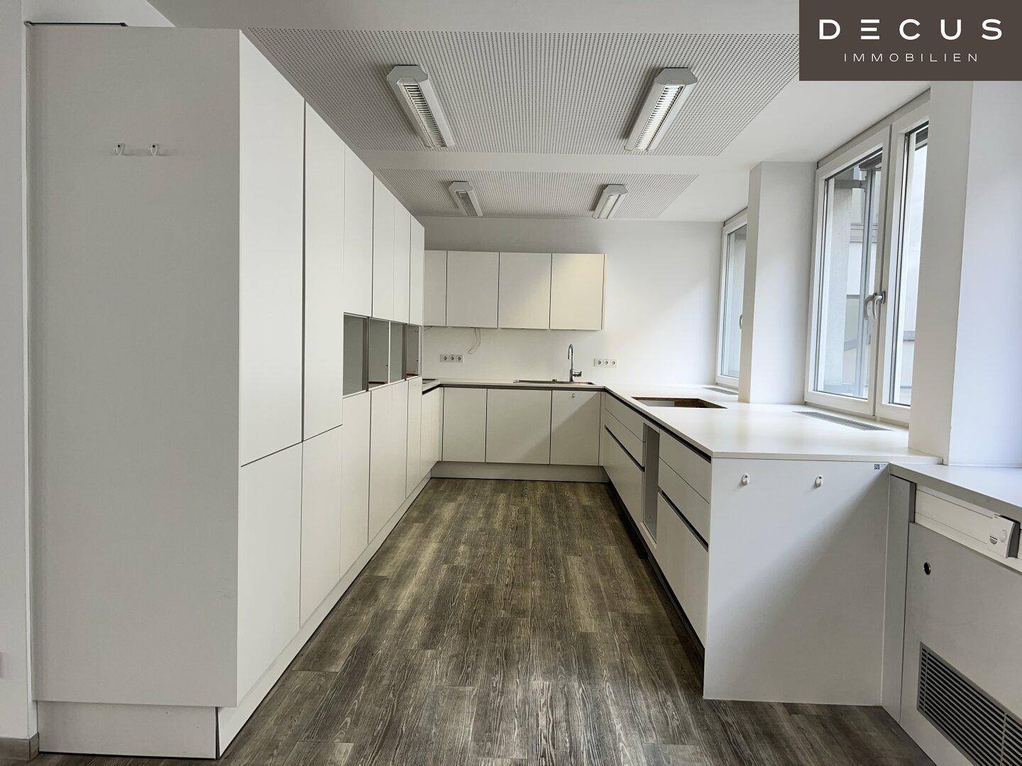 Moderne Küchenzeile mit weißen Schränken und Spüle in einem hellen Bürobereich, praktisch und funktional.