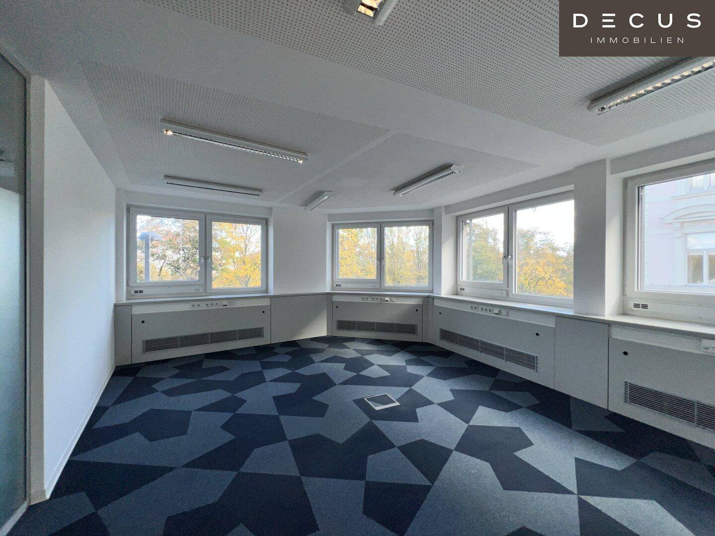 Geräumiges Büro mit mehreren Fenstern und einem modernen Teppichboden in geometrischem Muster.