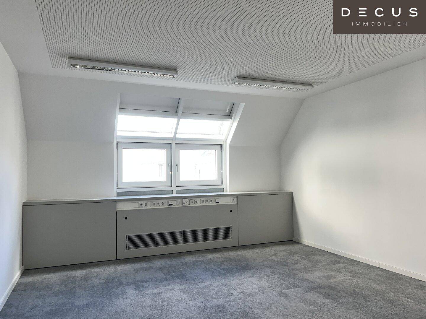 Dachgeschossbüro mit schrägen Wänden, Dachfenstern und integrierten Heizkörpern unter den Fenstern.