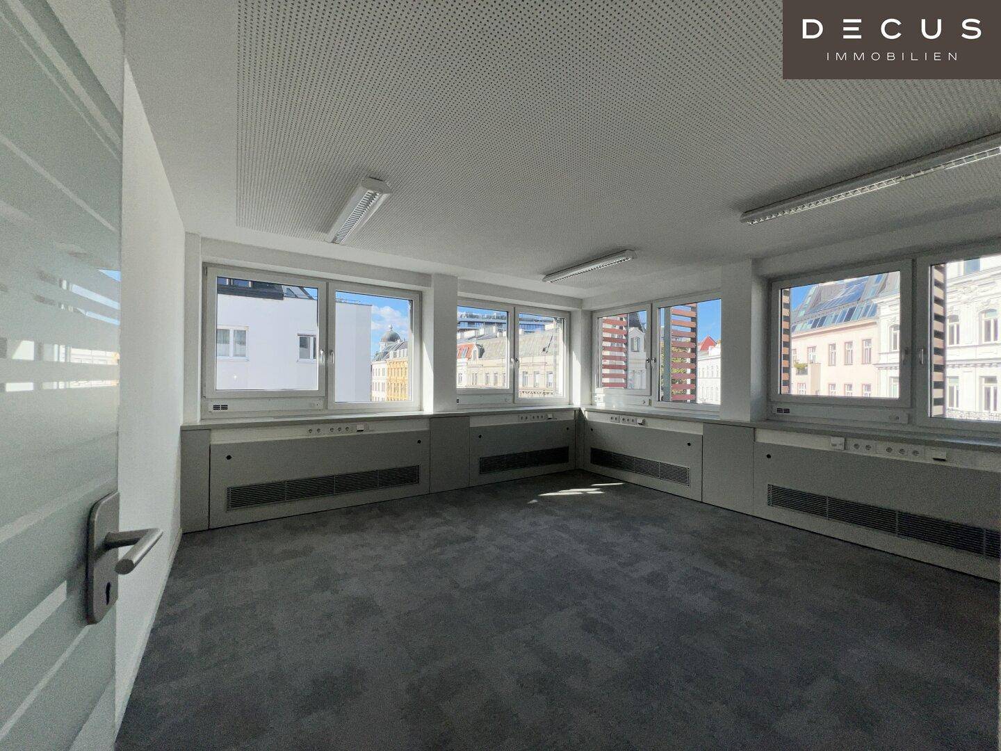 Geräumiges Büro mit Teppichboden, vielen Fenstern und moderner Deckenbeleuchtung.
